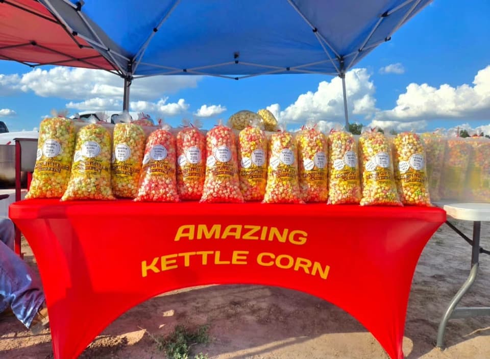 Bags of kettle corn lined up on a red Amazing Kettle Corn table under a canopy, at Coyoteville in Alice, Texas