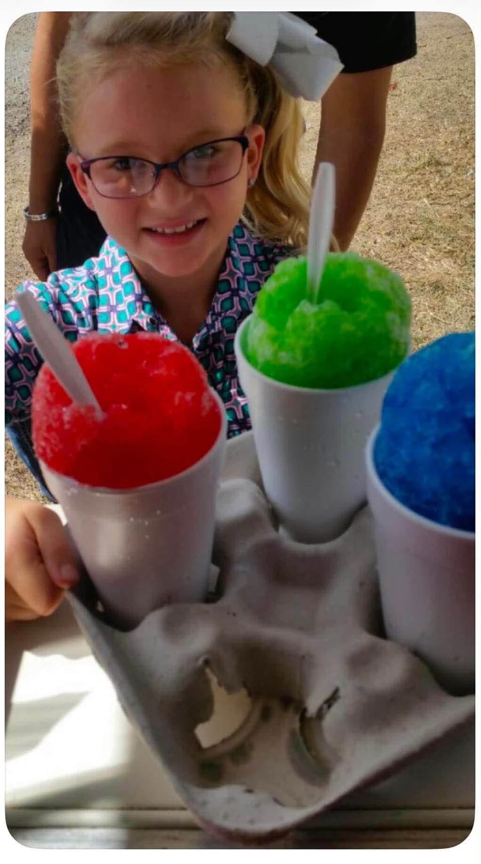 A girl holding a tray of red, green and blue shaved ice cups, at Coyoteville in Alice, Texas